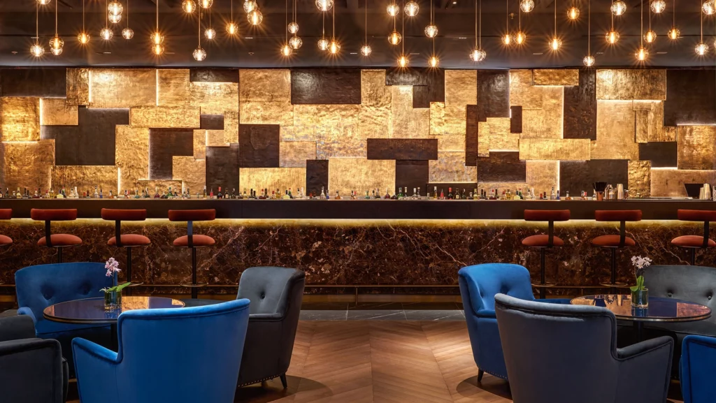 Bancone da bar dell'Hilton Rome EUR La Lama con pareti dorate e lampade che scendono dal soffitto. Tavoli e sedute blu