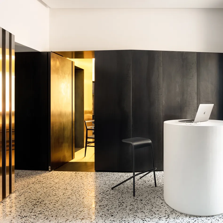 Interni della clinica Sotherga con boiserie in legno scuro Antonacci Falegnamerie, pareti dorate e bancone cilindrico bianco