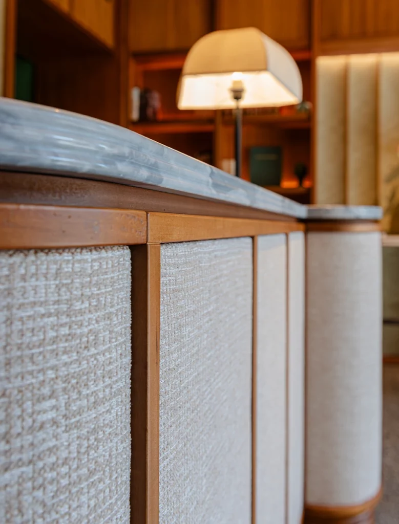 Dettaglio bancone rivestito in tessuto chiaro con piano in marmo e lampada da tavolo