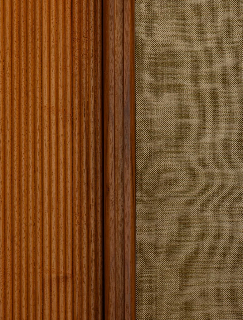 Accostamento materico tra pannello in legno scanalato e rivestimento tessile beige.