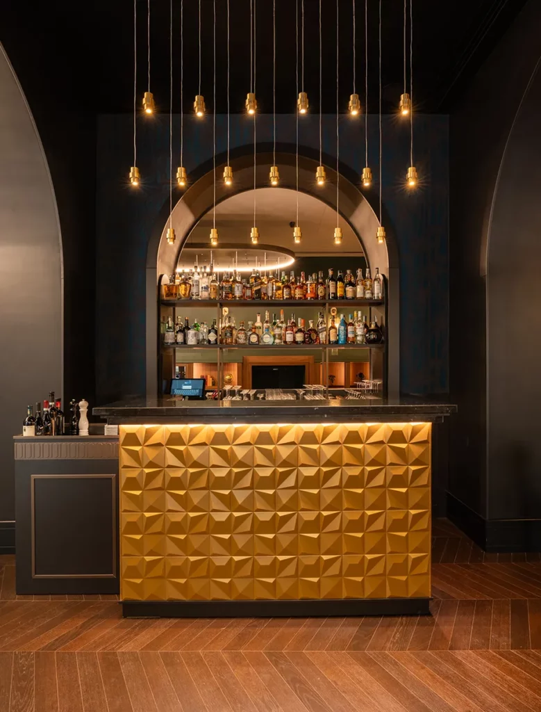 Bancone bar con rivestimento dorato tridimensionale e retroilluminato, sospensioni luminose a filo