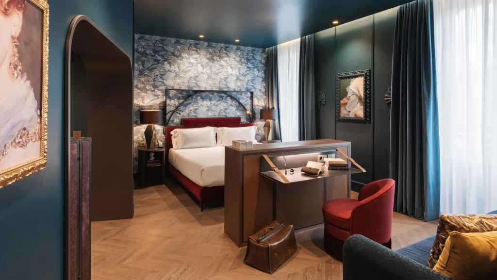 Camera matrimoniale con carta da parati a motivi orientali, scrivania in legno e poltrona rossa