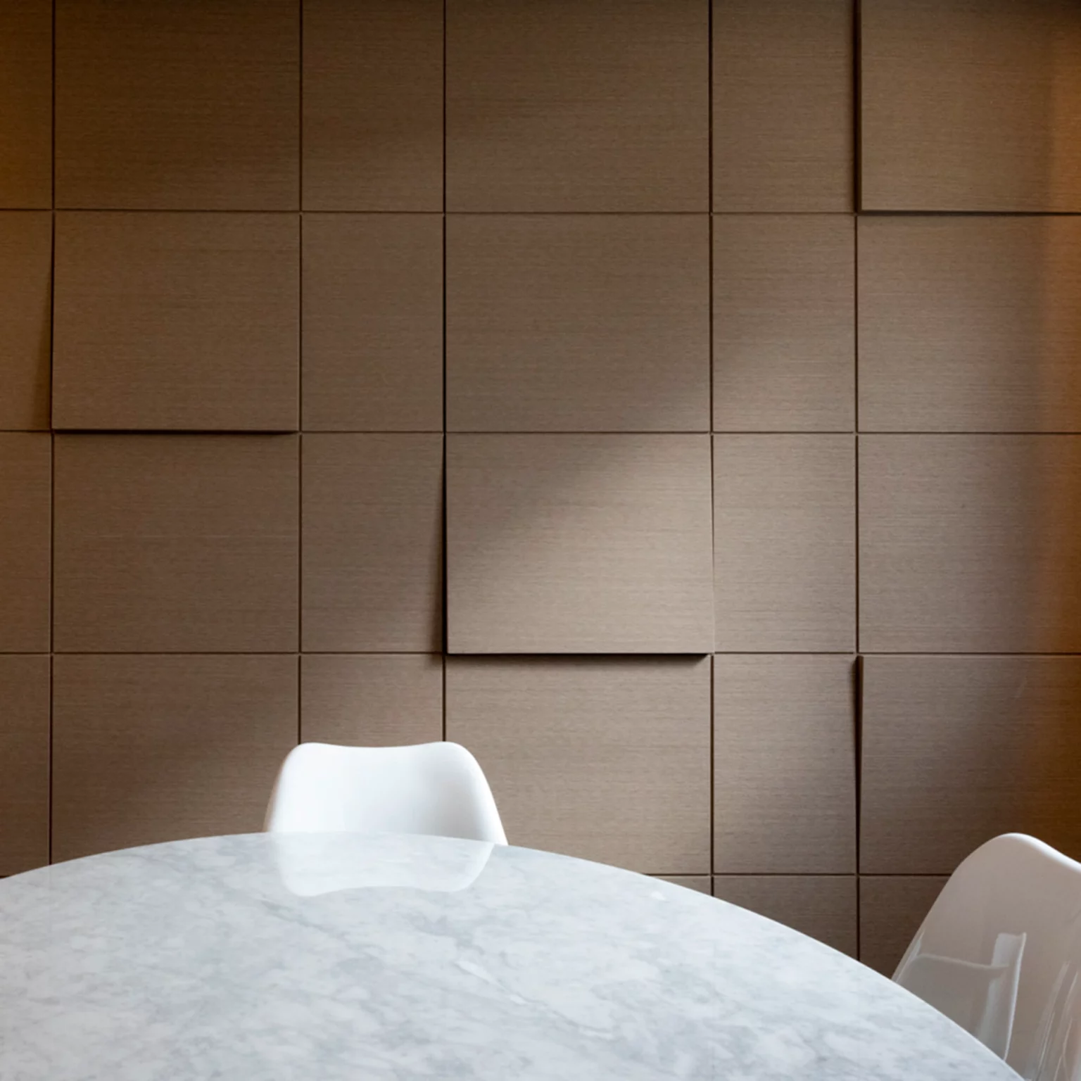 Boiserie in legno con pannelli geometrici a rilievo e tavolo in marmo con sedie bianche