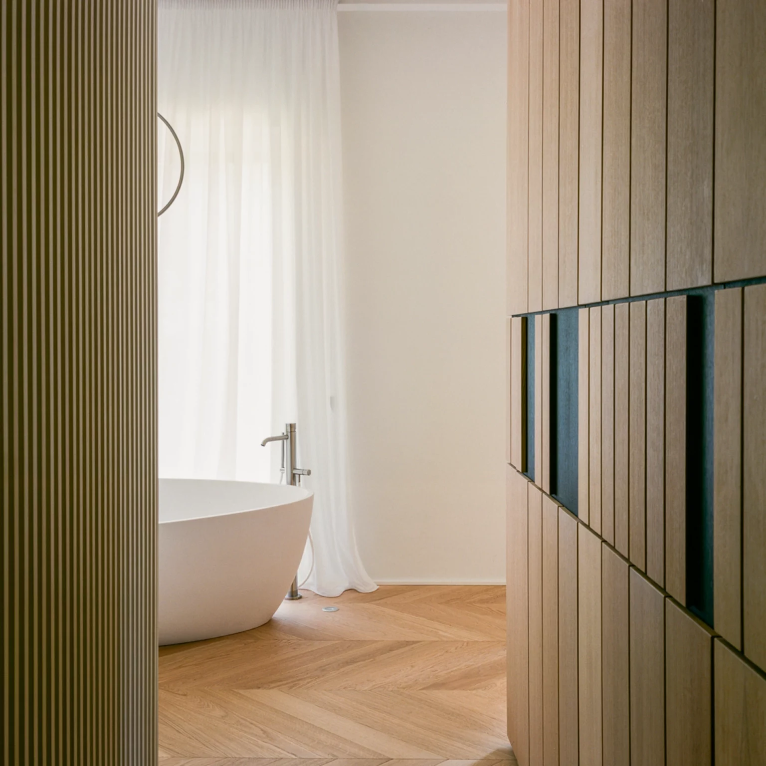 Interno bagno con rivestimenti in legno realizzati da falegnameria artigianale, pannelli su misura e pavimento in legno a spina di pesce, accanto a una vasca