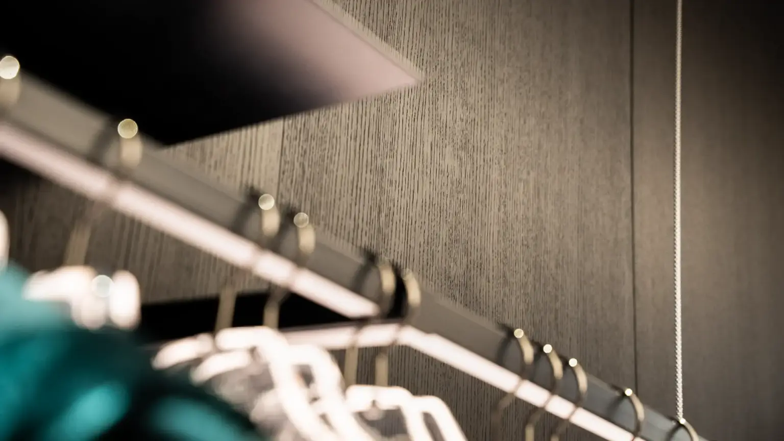 Detail of dark wood panelling with vertical grain and satin-finish metal coat hooks in the foreground inside the CiaoGym Store